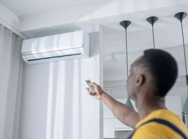 A man uses a remote to turn on his mini split air conditioner mounted high up on the wall of his home.