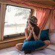 A young asian woman relaxes in the bunk of a vintage motorhome wearing a cheetah print bowler hat.