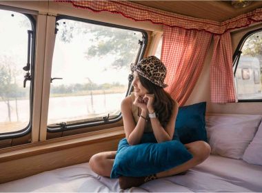 A young asian woman relaxes in the bunk of a vintage motorhome wearing a cheetah print bowler hat.