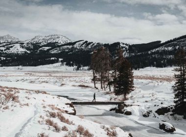 A visitor walks across a bridge over a stream in Yellowstone National Park in the winter.