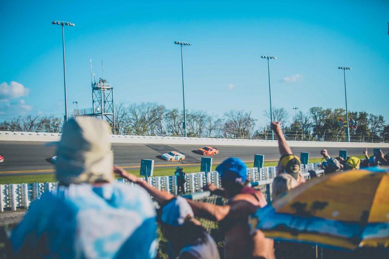 Fans cheering from the infield at the Daytona 500 on a sunny afternoon.