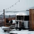 A shiny aluminum Airstream travel trailer parked at the top of a snowy hill overlooking the valley below.