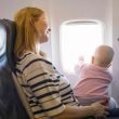 A mother holds her baby on her lap as she looks out the window of the plane.