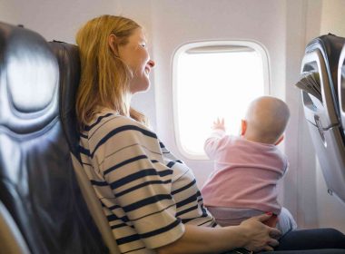 A mother holds her baby on her lap as she looks out the window of the plane.