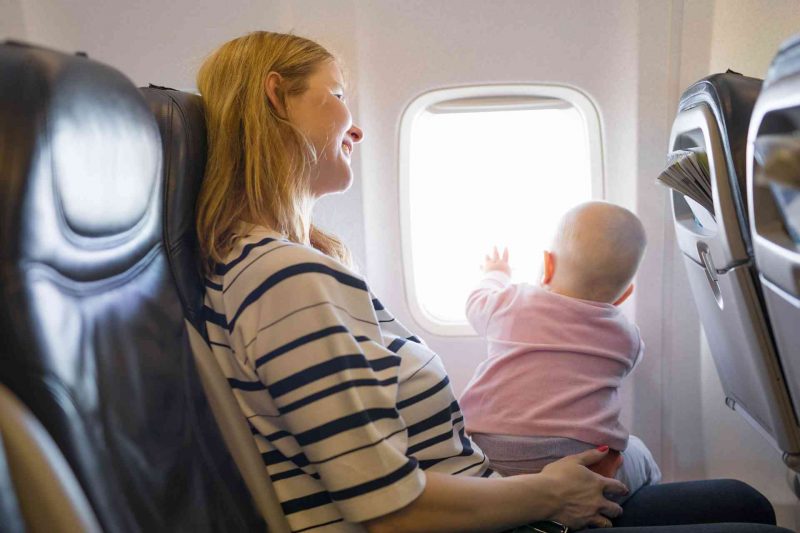 A mother holds her baby on her lap as she looks out the window of the plane.