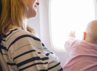 A mother holds her baby on her lap as she looks out the window of the plane.