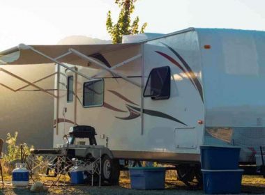 An RV parked on a hill with the sun setting behind the awning.