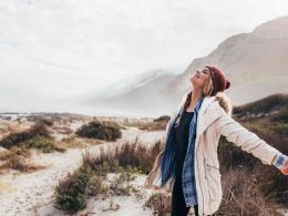 A woman happily breathes in fresh air down my the sea.