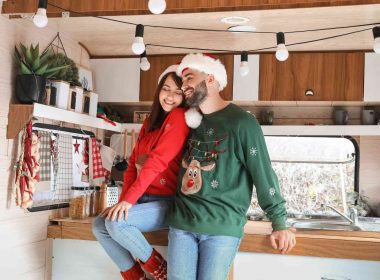 A couple adorned in Christmas sweaters and Santa hats having fun in their RV.