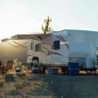 An RV parked on a hill with the sun setting behind the awning.