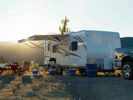 An RV parked on a hill with the sun setting behind the awning.