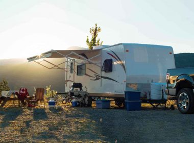 An RV parked on a hill with the sun setting behind the awning.