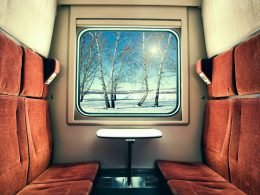 Inside the private cabin of a sleeper train rolling by a wintry landscape.