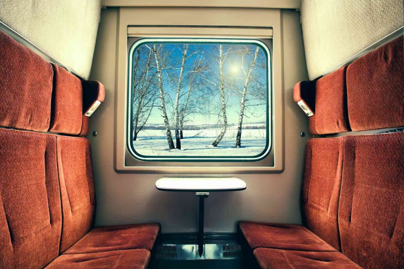 Inside the private cabin of a sleeper train rolling by a wintry landscape.