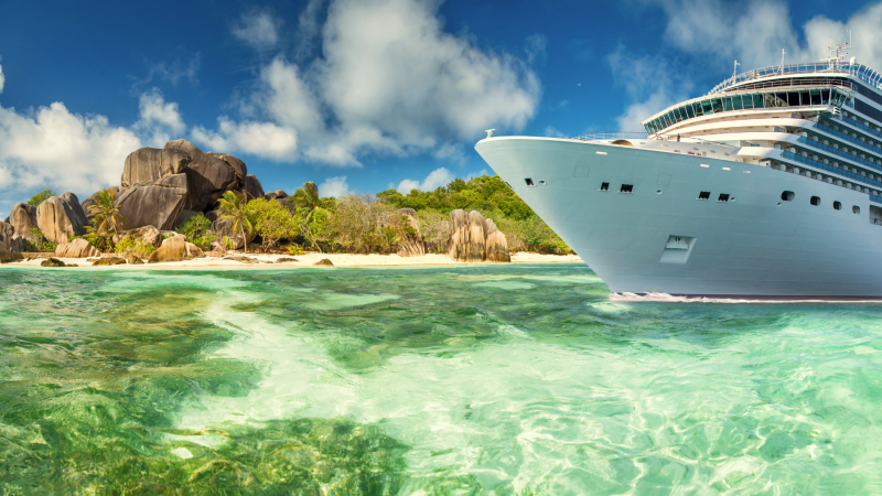 Cruise ship in aqua waters in front of a rocky island.