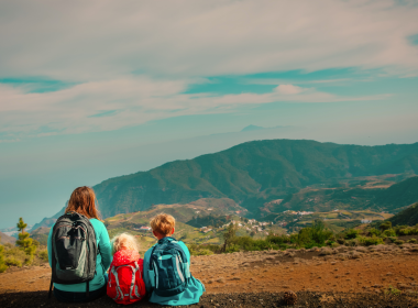 Mother and two children traveling and looking at mountain views as they sit on the ground.