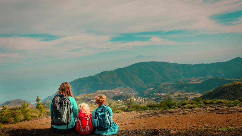 Mother and two children traveling and looking at mountain views as they sit on the ground.