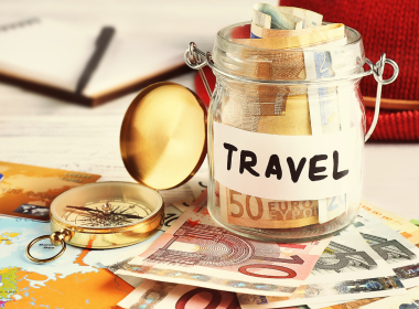 A travel savings jar with international money in it and a compass lying beside it.