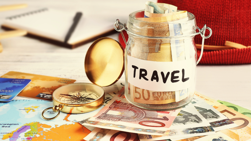 A travel savings jar with international money in it and a compass lying beside it.