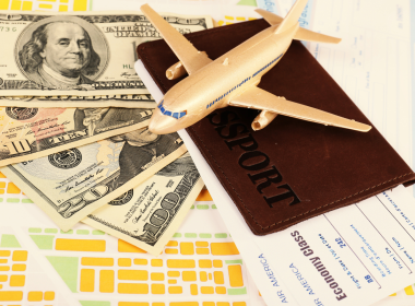 Toy airplane sitting atop a passport, plane ticket, and $130 in cash.