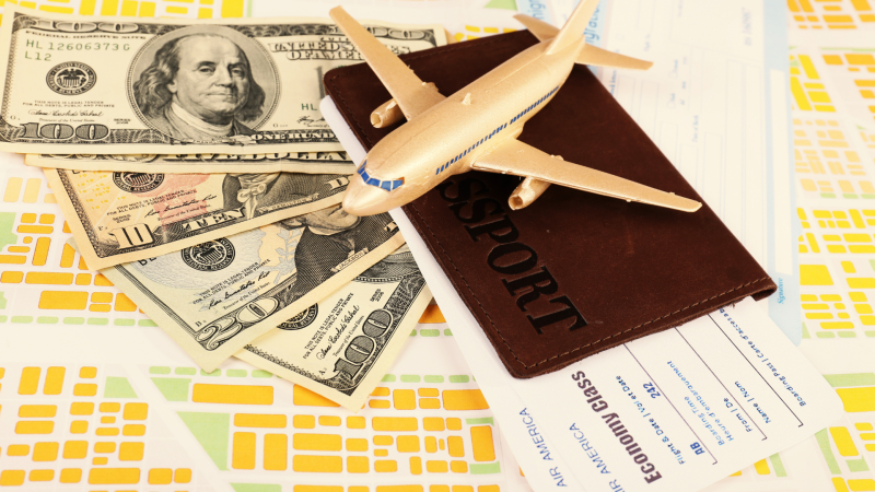 Toy airplane sitting atop a passport, plane ticket, and $130 in cash.