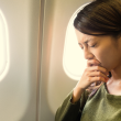 Woman holding her eyes shut tightly while seated on an airplane.