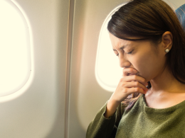 Woman holding her eyes shut tightly while seated on an airplane.