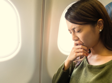 Woman holding her eyes shut tightly while seated on an airplane.