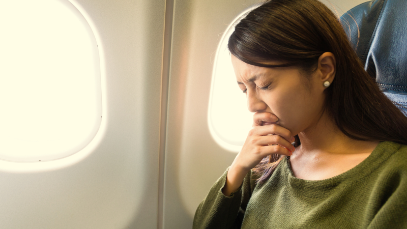 Woman holding her eyes shut tightly while seated on an airplane.