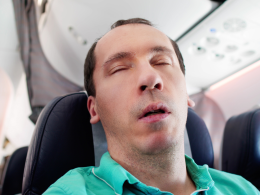 Man sleeping on a plane wrong in a teal shirt and no neck pillow.