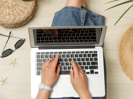 Person on laptop with beach gear laid out around them.