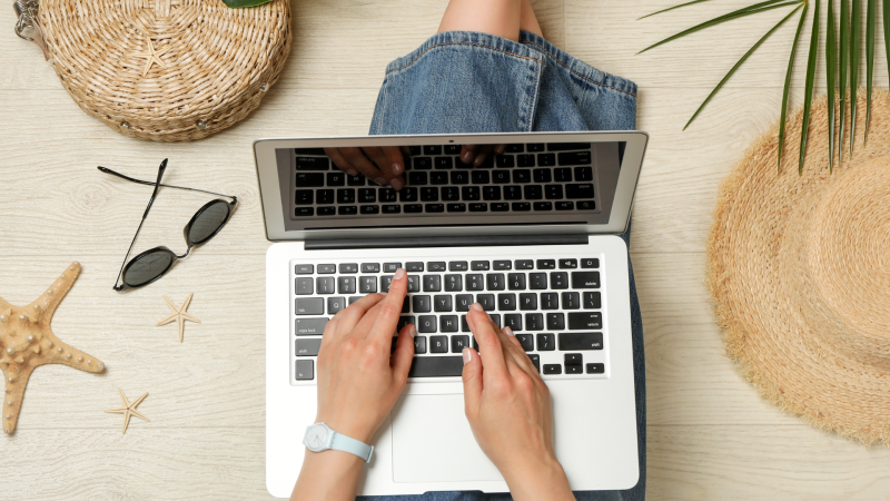 Person on laptop with beach gear laid out around them.