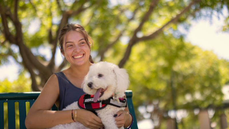 Woman holding service dog while sitting on a bench outside.