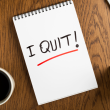 "I QUIT!" wirtten on a notepad on a desk between a mug of coffe and pens.