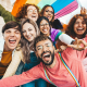 A group of seven people happily taking a photo together with an lgbtq+ flag in the background.