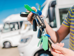 Person holding keys in front of a lot of RV's.