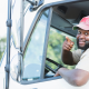 A person smiling and pointing at the camera as they hang out of their truck window.