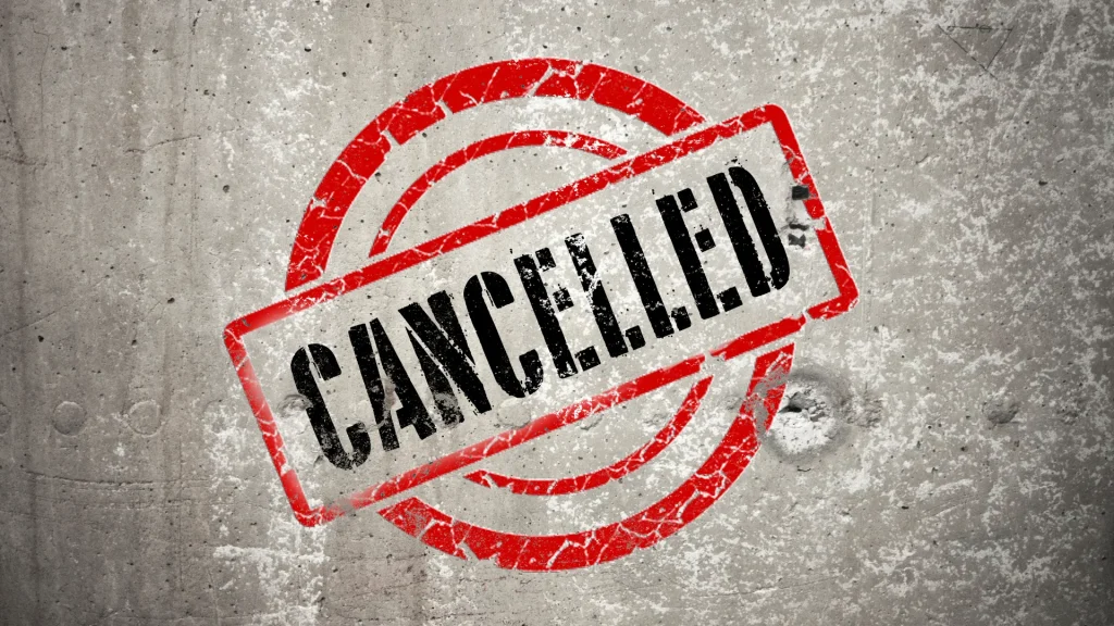 A concrete backdrop with a chipped painted sign saying "CANCELLED", wrapped in a red outlined rectangle as two circles sit behind it, resembling a target.