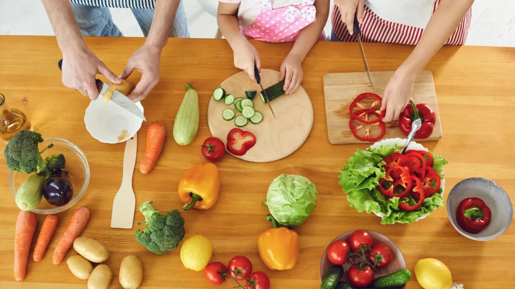 Three people cutting up veggies at a butcher block counter top. Representing how Today is Someday is prioritizing home-cooked meals to counter how full-time travel ruined Today is Someday.