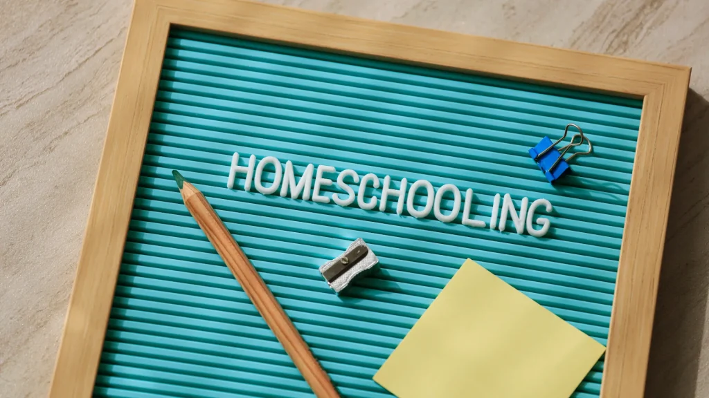 A blue wood framed letterboard with the word "homeschooling" on it along with a pencil, a pencil sharpener, a notepad, and clip. 