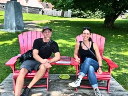 Irene Iron Travels - Chris and Aaron sitting in red outdoor chairs surrounded by a lush grassy lawn.