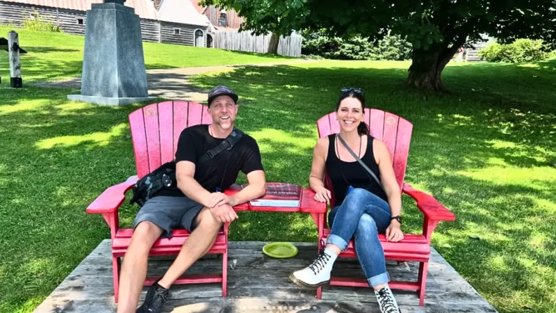Irene Iron Travels - Chris and Aaron sitting in red outdoor chairs surrounded by a lush grassy lawn.