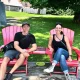 Irene Iron Travels - Chris and Aaron sitting in red outdoor chairs surrounded by a lush grassy lawn.