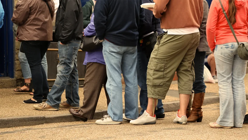 A close up photo of the lower halves of 10+ people standing in a long line.