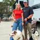 Wild RV Life and their two dogs as they pose for a photo beside their RV.