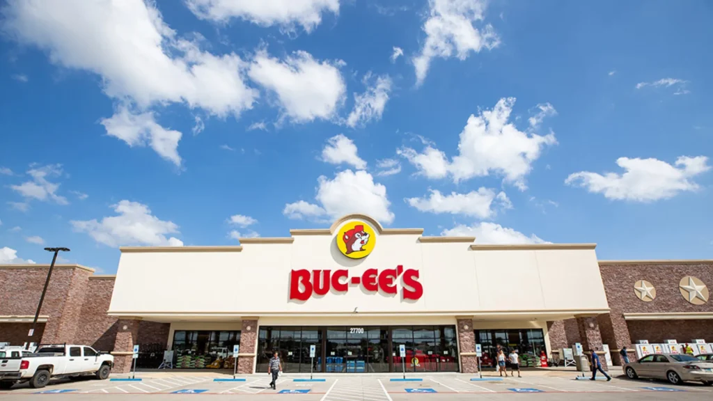 The storefront of a Buc-ee's with a bright blue sky dotted with clouds above it. 