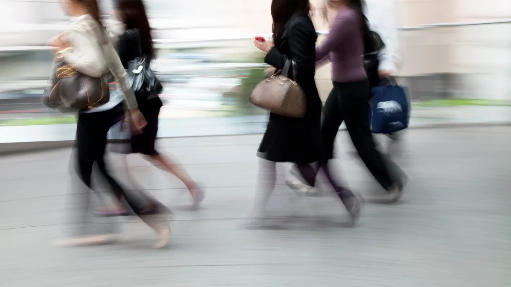 A group of people rushing in a motion-blurred photo as five people walk by outside.
