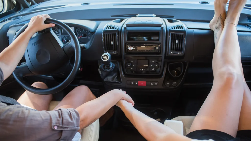 A couple in the front seat of their camper as they hold hands and drive. 