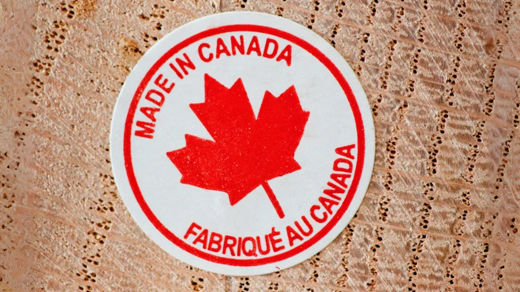 A woodgrain background with a "MADE IN CANADA" sticker. The sticker is white with a red border with a red maple leaf in the center as "MADE IN CANADA" wraps above it and "FABRIQUE AU CANADA" wraps beneath it.