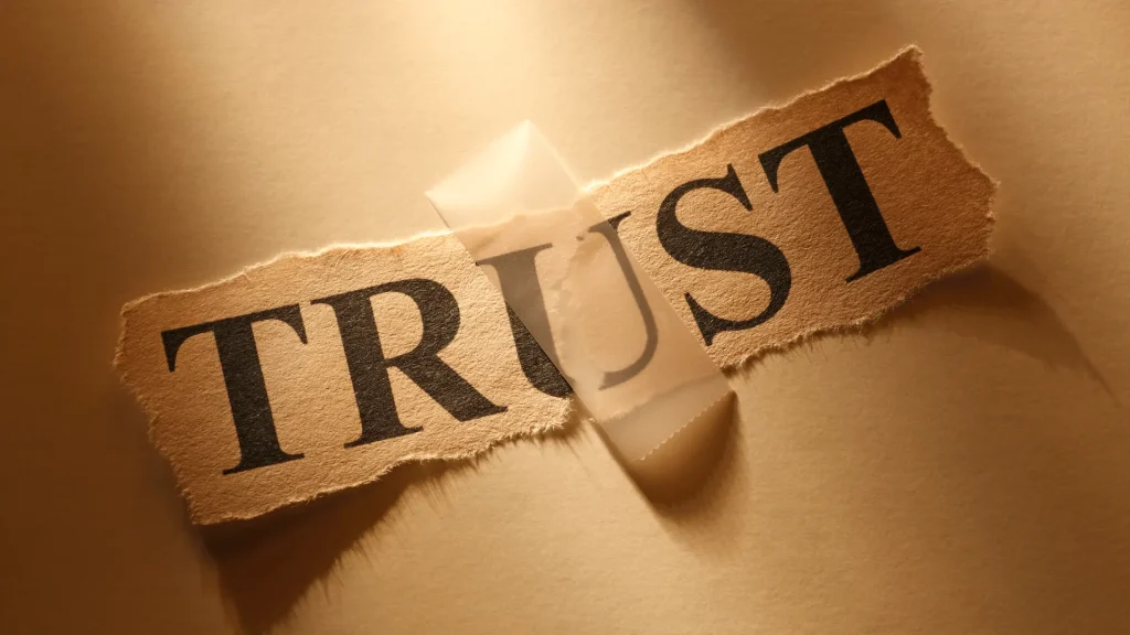 Trust on brown torn paper, that is torn in the middle affixed with a piece of scotch tape against a brown background.